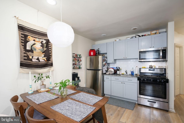 kitchen with sink, hanging light fixtures, light hardwood / wood-style flooring, tasteful backsplash, and stainless steel appliances