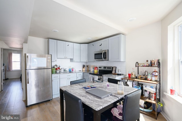 kitchen with light stone countertops, backsplash, stainless steel appliances, and light hardwood / wood-style floors