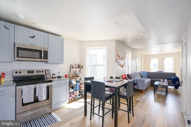 kitchen with decorative backsplash, light stone counters, light hardwood / wood-style flooring, and appliances with stainless steel finishes