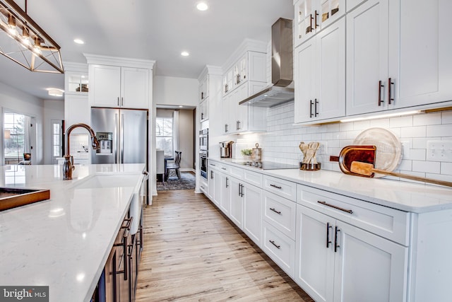 kitchen with wall chimney exhaust hood, light stone countertops, light wood-type flooring, decorative light fixtures, and white cabinetry