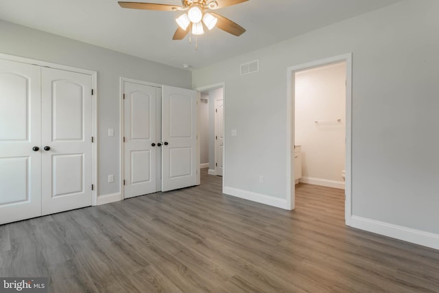 unfurnished bedroom with ceiling fan, wood-type flooring, and multiple closets