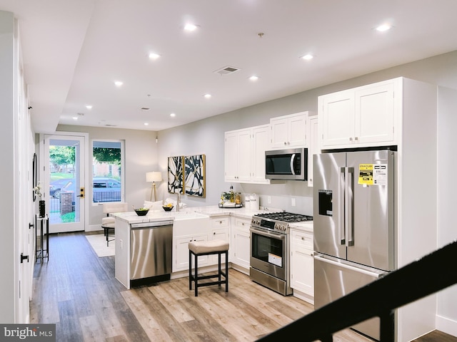 kitchen with white cabinetry, high quality appliances, kitchen peninsula, and light hardwood / wood-style flooring