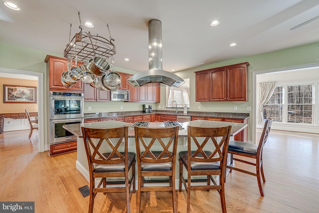 kitchen with island exhaust hood, appliances with stainless steel finishes, light wood-type flooring, a kitchen island, and a breakfast bar area