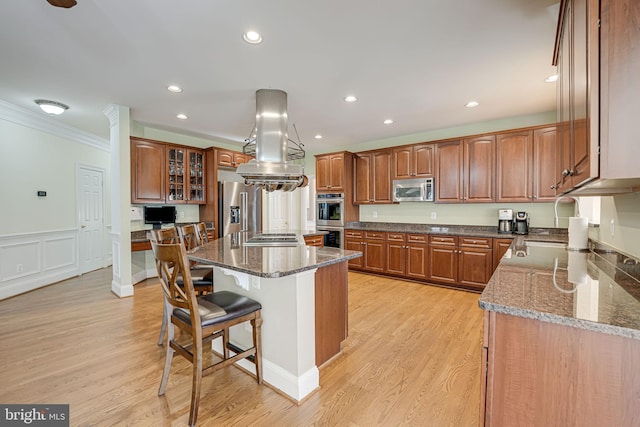 kitchen featuring appliances with stainless steel finishes, ornamental molding, island range hood, light hardwood / wood-style floors, and a kitchen island