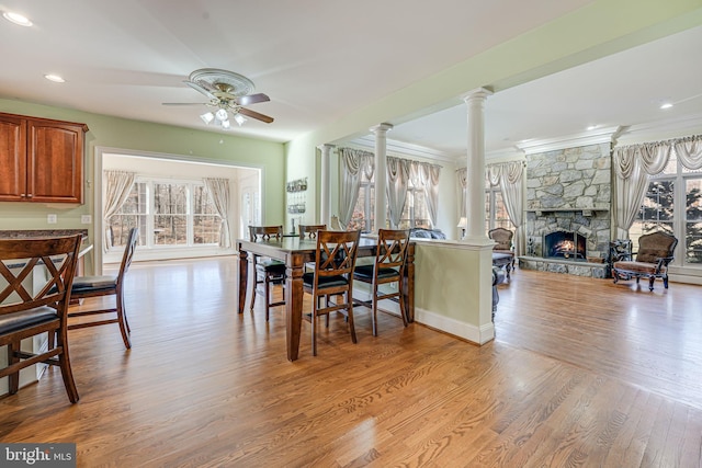 dining room with light hardwood / wood-style floors, a stone fireplace, a wealth of natural light, and decorative columns