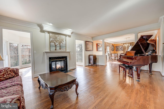 living room featuring ornate columns, an inviting chandelier, light hardwood / wood-style floors, and ornamental molding