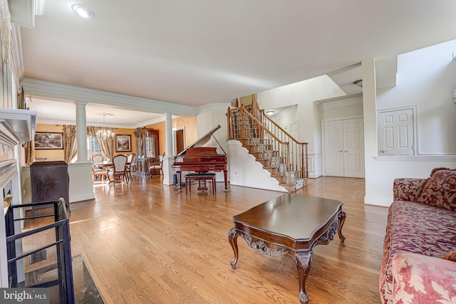 living room with ornate columns, crown molding, light hardwood / wood-style floors, and an inviting chandelier