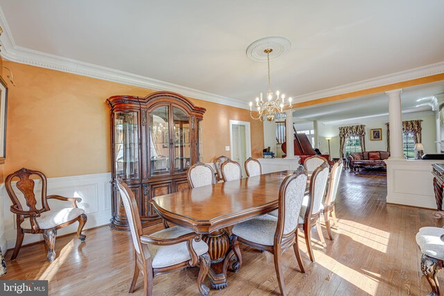 dining space featuring ornate columns, crown molding, an inviting chandelier, and light wood-type flooring