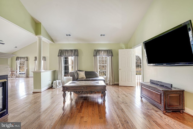 living room with ornate columns, light hardwood / wood-style flooring, and high vaulted ceiling