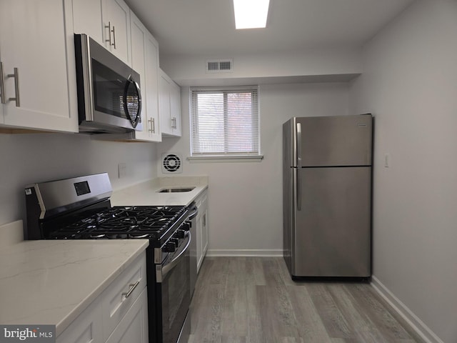 kitchen with light stone counters, white cabinetry, stainless steel appliances, and light hardwood / wood-style flooring