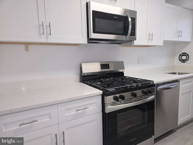 kitchen with light stone countertops, stainless steel appliances, sink, light hardwood / wood-style floors, and white cabinetry