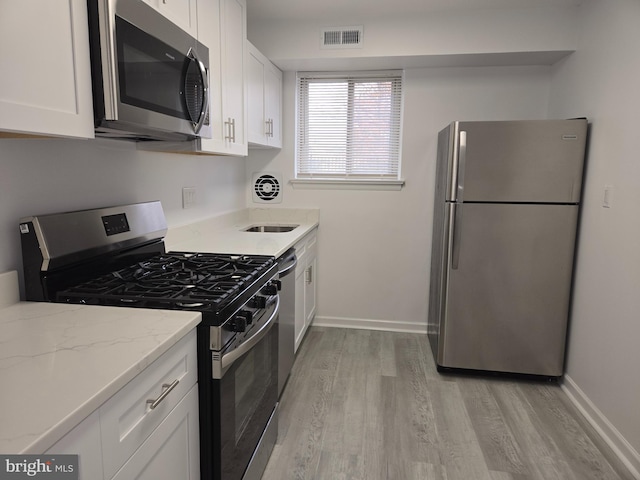 kitchen featuring light stone countertops, stainless steel appliances, white cabinetry, and light hardwood / wood-style floors