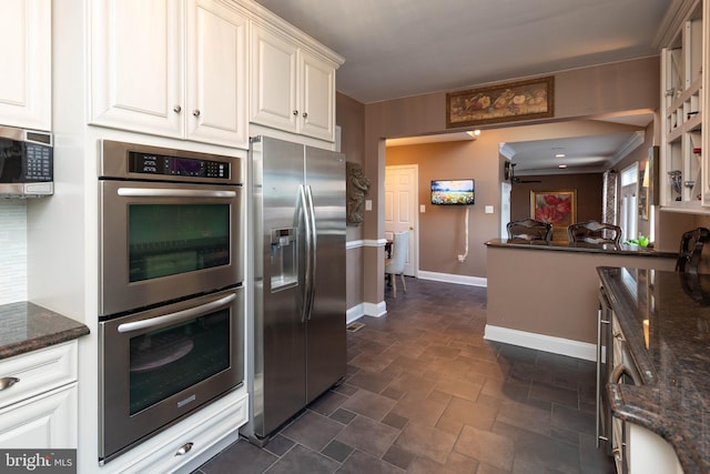 kitchen with appliances with stainless steel finishes, white cabinetry, ceiling fan, and dark stone countertops