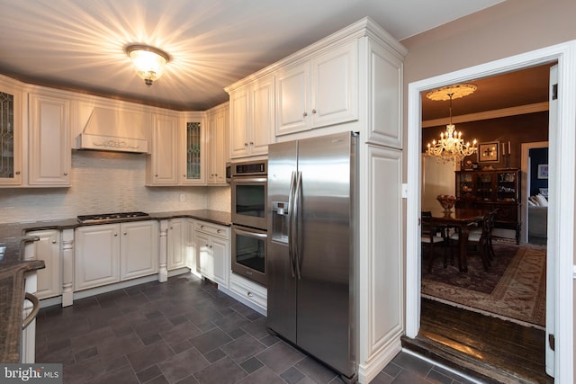 kitchen featuring backsplash, white cabinets, a notable chandelier, custom range hood, and stainless steel appliances