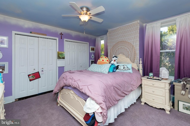 bedroom featuring ceiling fan, two closets, and dark colored carpet