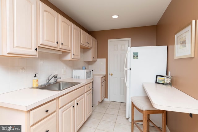 kitchen featuring white appliances, backsplash, sink, light tile patterned floors, and a breakfast bar area