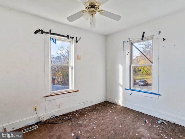 empty room with a wealth of natural light, ceiling fan, and dark carpet