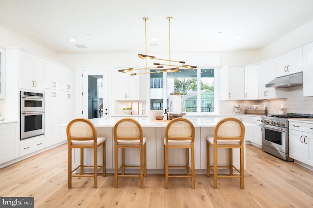 kitchen with white cabinetry, light hardwood / wood-style flooring, stainless steel appliances, and decorative light fixtures