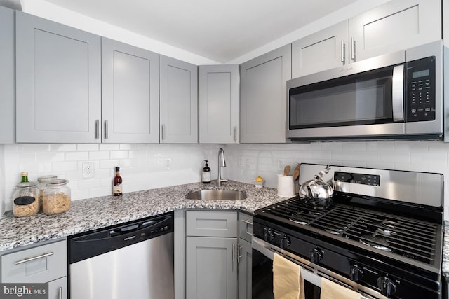 kitchen with sink, gray cabinets, tasteful backsplash, light stone counters, and stainless steel appliances