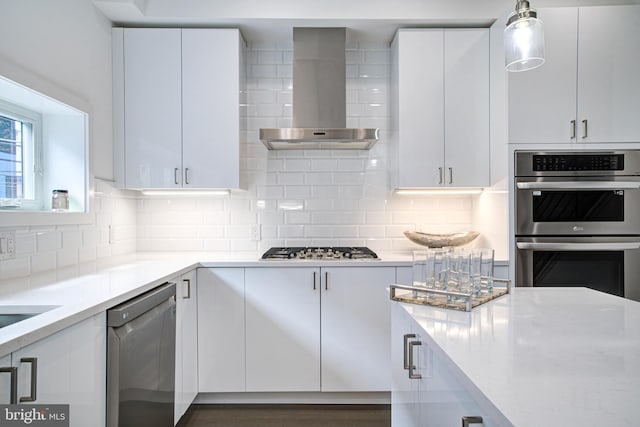 kitchen with white cabinetry, wall chimney exhaust hood, stainless steel appliances, decorative light fixtures, and decorative backsplash