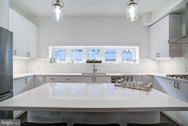 kitchen featuring sink, wall chimney range hood, gas cooktop, decorative light fixtures, and a breakfast bar