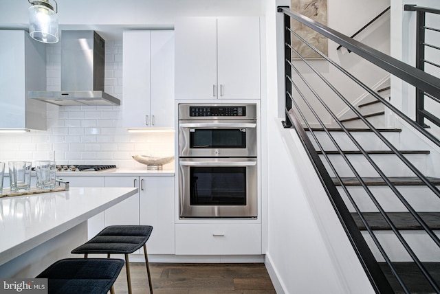 kitchen with wall chimney range hood, dark hardwood / wood-style floors, appliances with stainless steel finishes, tasteful backsplash, and white cabinetry