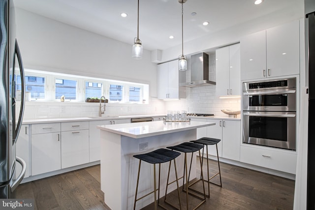 kitchen with stainless steel appliances, white cabinetry, wall chimney exhaust hood, and sink