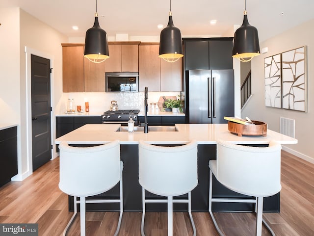 kitchen with hanging light fixtures, an island with sink, stainless steel appliances, and light wood-type flooring