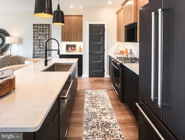 kitchen featuring black appliances, sink, an island with sink, decorative light fixtures, and wood-type flooring