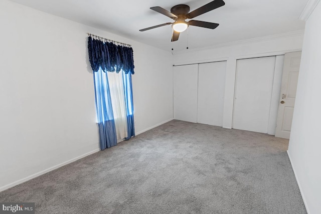 unfurnished bedroom featuring carpet flooring, ceiling fan, crown molding, and two closets