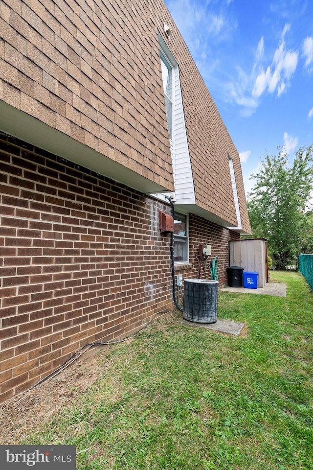 view of side of property with a lawn, cooling unit, and a shed