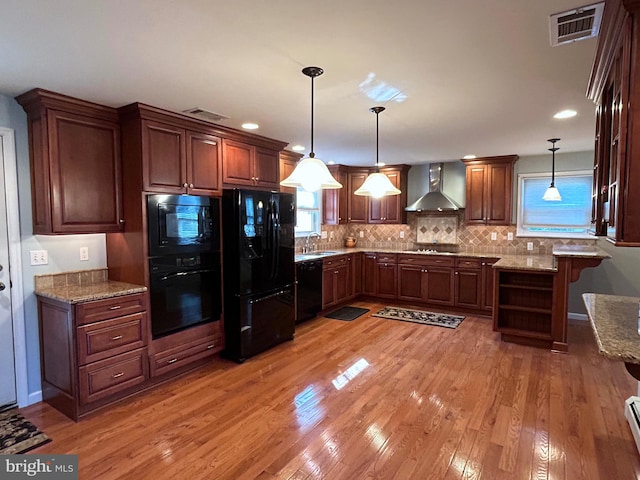 kitchen featuring pendant lighting, black appliances, wall chimney range hood, light hardwood / wood-style flooring, and light stone counters