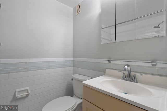 bathroom featuring vanity, toilet, and tile walls