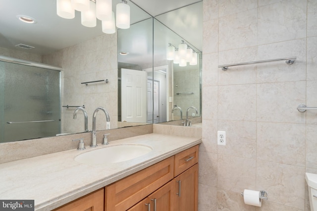 bathroom featuring a shower with door, vanity, tile walls, and toilet