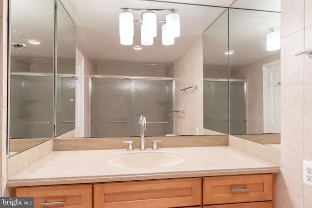 bathroom with vanity, a shower with shower door, and tile walls