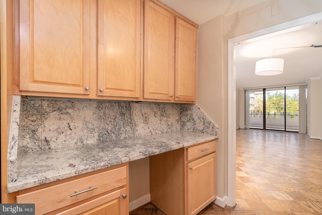 kitchen featuring light stone counters, built in desk, backsplash, and light brown cabinetry