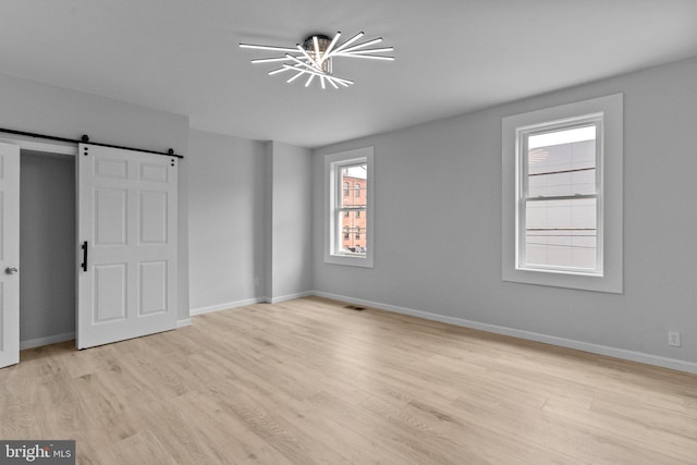 spare room featuring a barn door, a notable chandelier, and light wood-type flooring