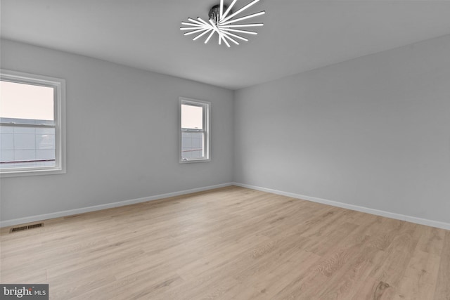 spare room with light hardwood / wood-style floors, a wealth of natural light, and a chandelier