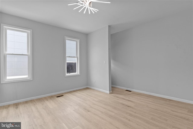 spare room with a wealth of natural light, light hardwood / wood-style flooring, and a notable chandelier