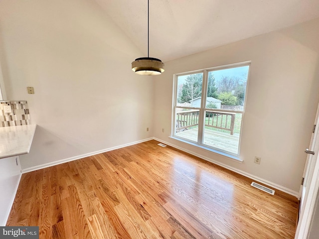 unfurnished dining area featuring light wood-type flooring and vaulted ceiling