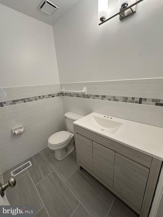 bathroom with tile patterned floors, vanity, toilet, and tile walls