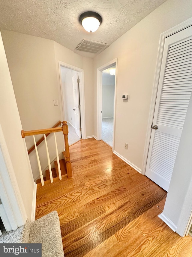 hallway with a textured ceiling and light hardwood / wood-style flooring