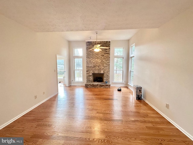 unfurnished living room with ceiling fan, a fireplace, wood-type flooring, and a textured ceiling