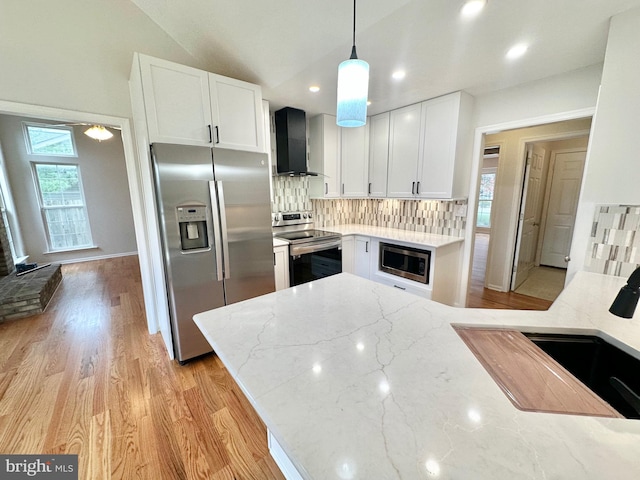 kitchen featuring lofted ceiling, white cabinets, wall chimney range hood, decorative backsplash, and appliances with stainless steel finishes