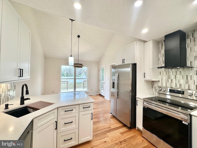 kitchen featuring lofted ceiling, wall chimney range hood, sink, appliances with stainless steel finishes, and white cabinetry