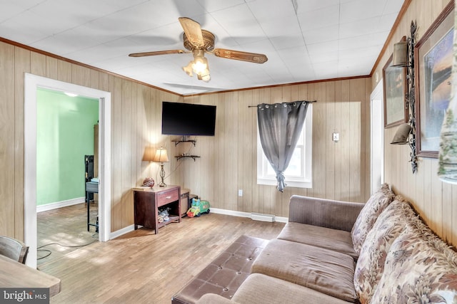 living room featuring ornamental molding, light hardwood / wood-style floors, ceiling fan, and wooden walls