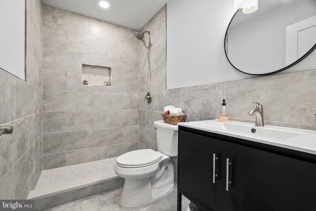 bathroom featuring vanity, toilet, tiled shower, and tile walls