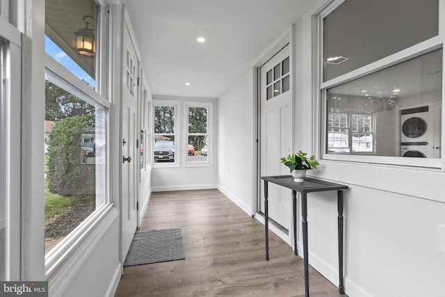 doorway to outside with stacked washing maching and dryer and hardwood / wood-style flooring