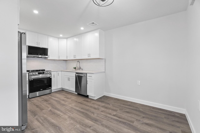 kitchen with sink, backsplash, wood-type flooring, white cabinets, and appliances with stainless steel finishes