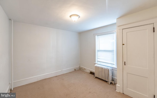 spare room with radiator and light carpet